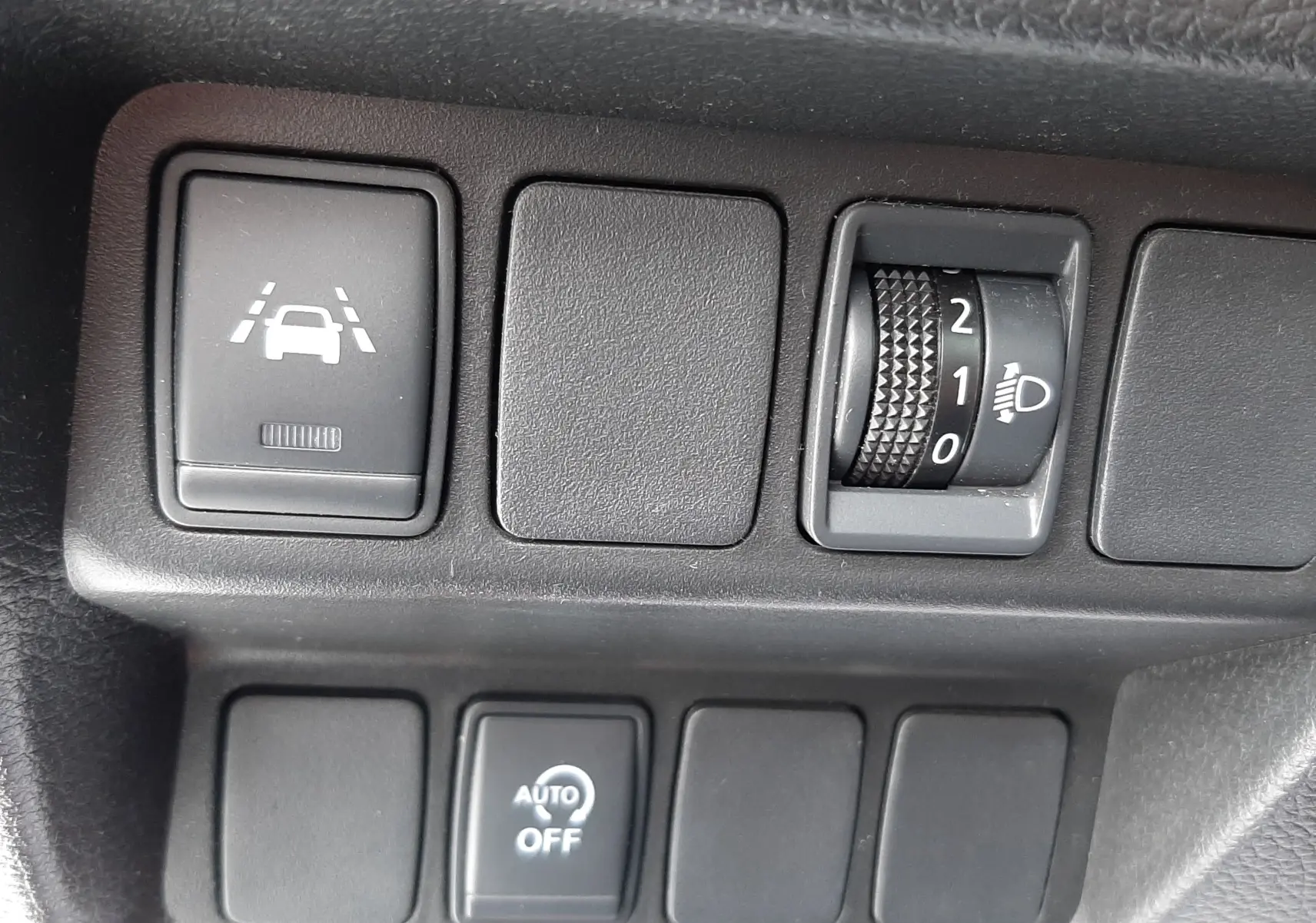 Gros plan sur les commandes de régulation d'éclairage et d'assistance au maintien de voie du Nissan Qashqai blanc 2020.