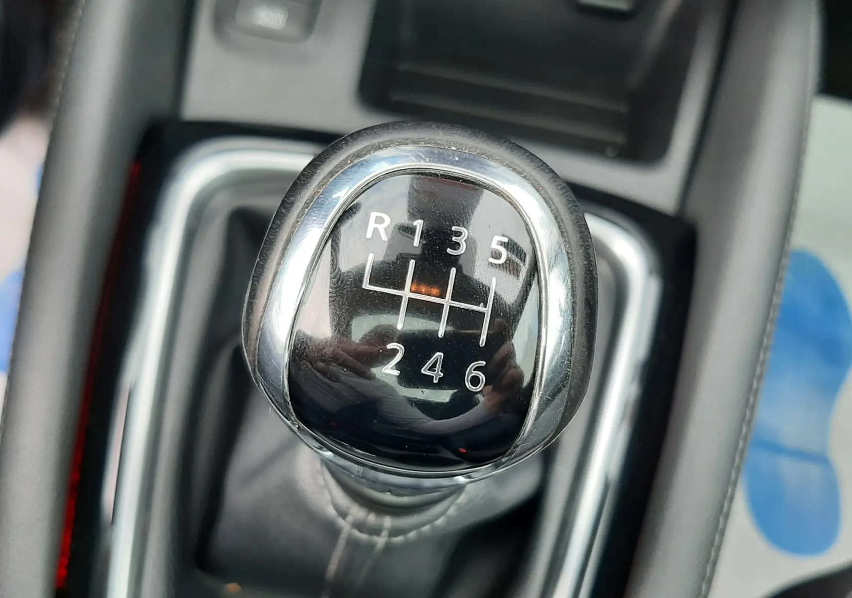 Gros plan sur le levier de vitesse manuel chromé du Nissan Qashqai blanc, avec coutures visibles sur la soufflet en cuir noir.