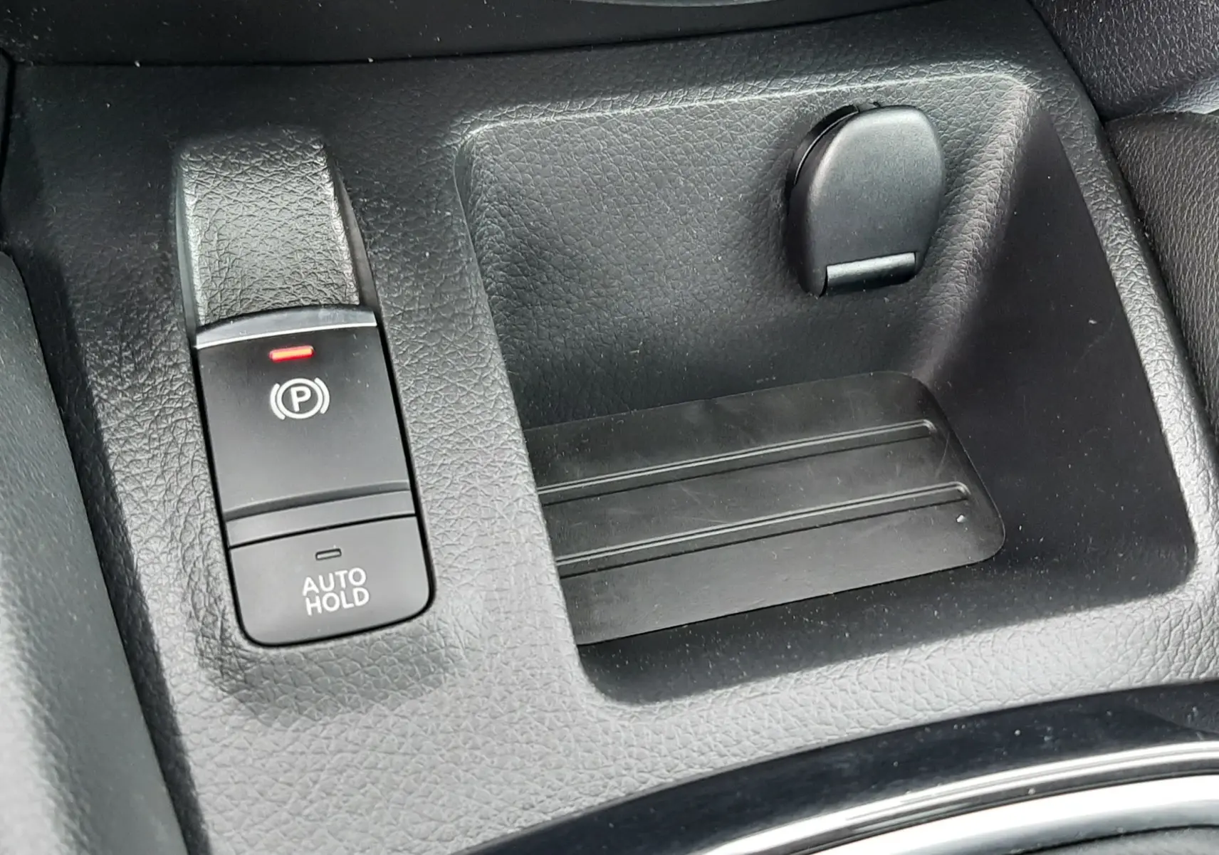 Gros plan sur la console centrale noire du Nissan Qashqai 1.5 DCI 115CH N-Connecta avec frein à main électronique et rangement.