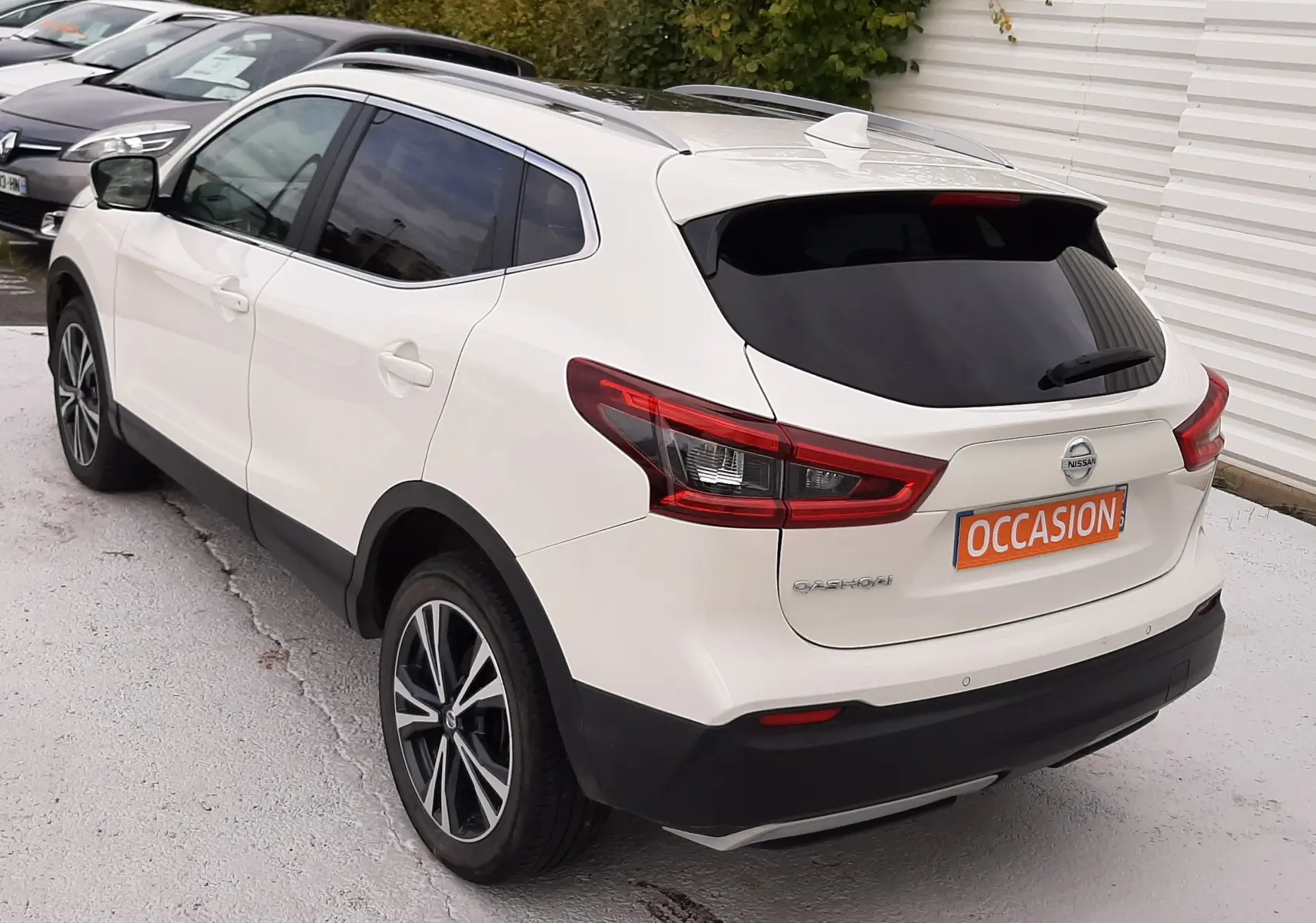 Vue 3/4 arrière droite d'un Nissan Qashqai blanc avec vitres teintées et jantes alliage bicolores.
