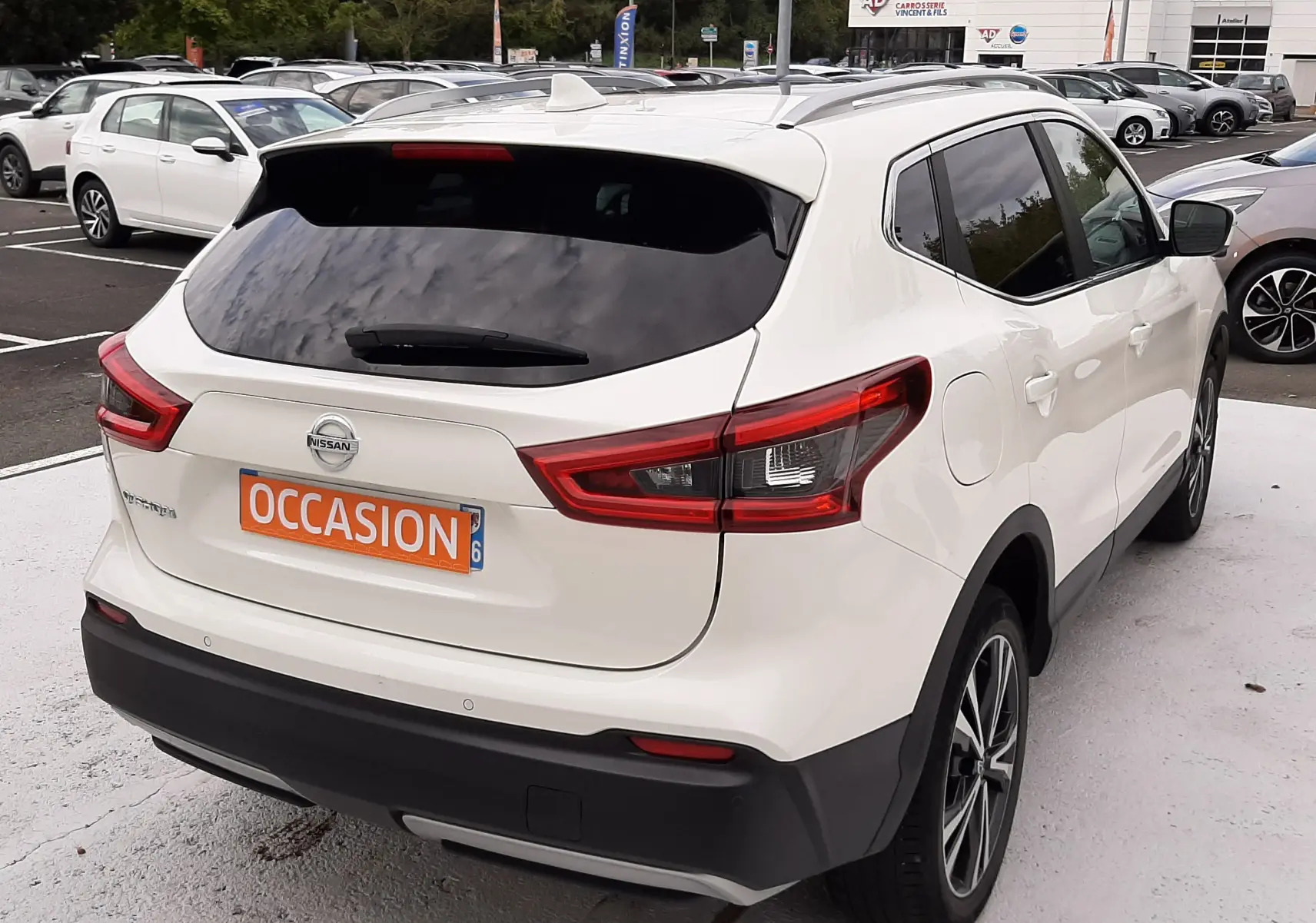 Vue 3/4 arrière droite d'un Nissan Qashqai blanc 2020 avec vitres teintées et toit équipé de barres de toit.