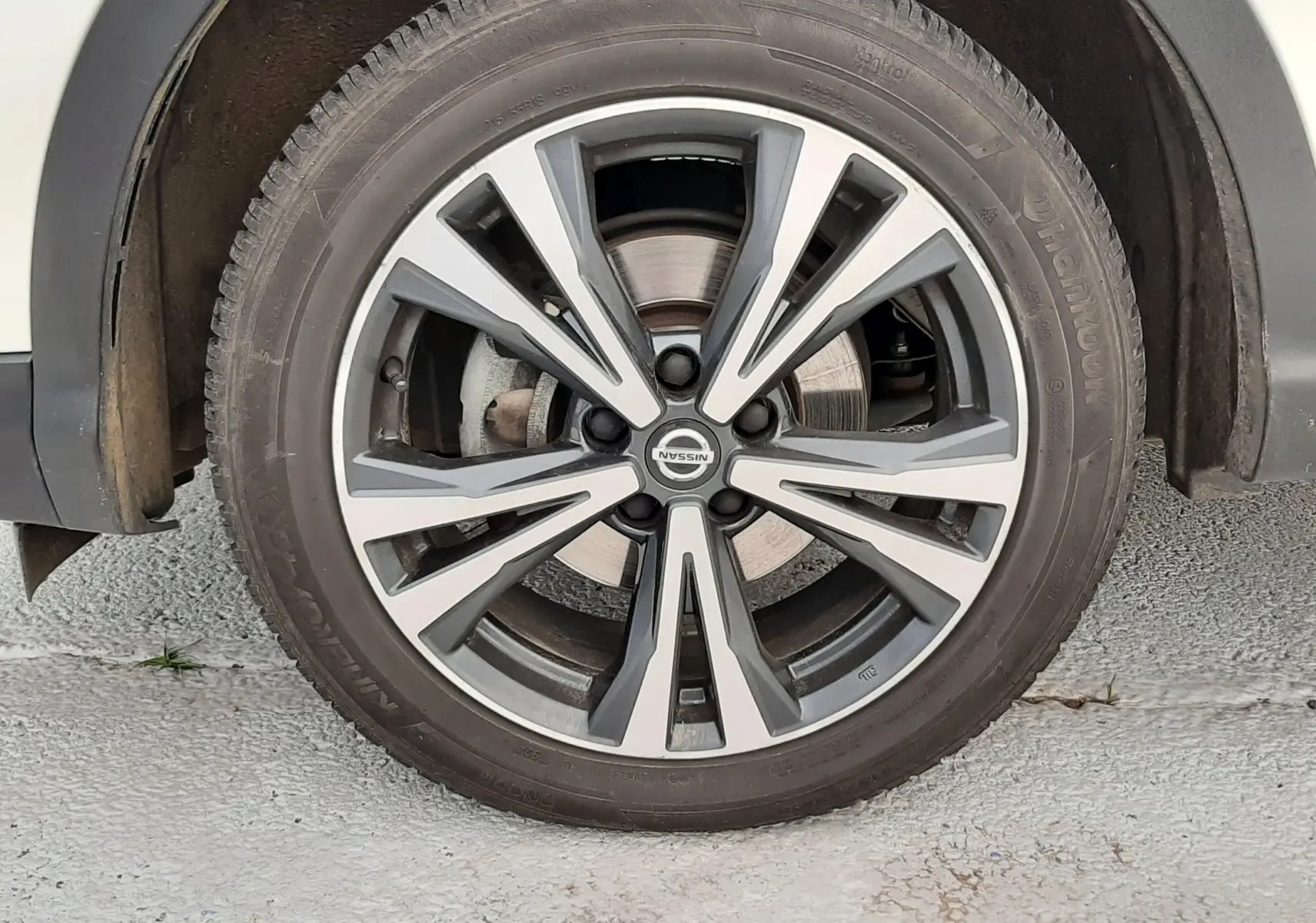 Gros plan sur la roue avant droite d'un Nissan Qashqai blanc, jante alliage bicolore au design moderne.