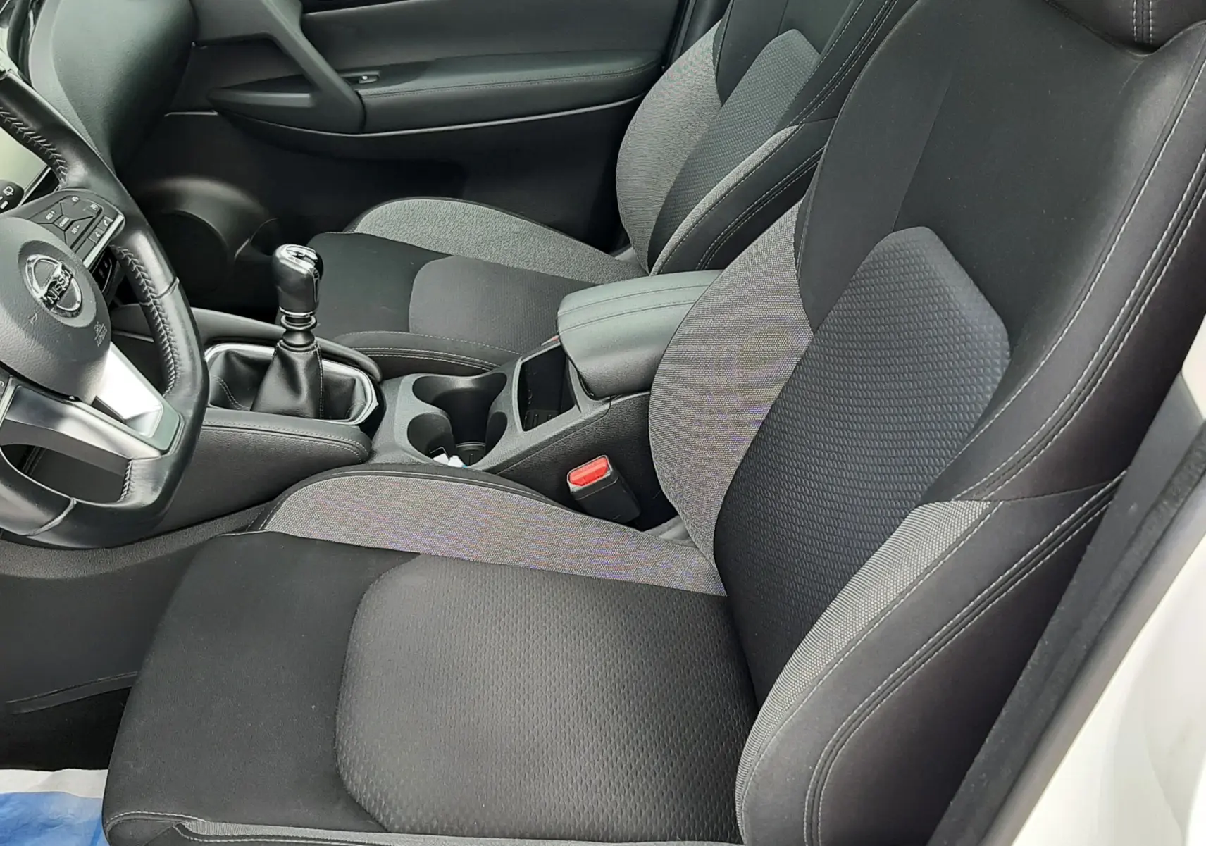 Vue intérieure côté conducteur du Nissan Qashqai 2020 blanc, sièges tissu noir et gris avec levier de vitesse manuel.