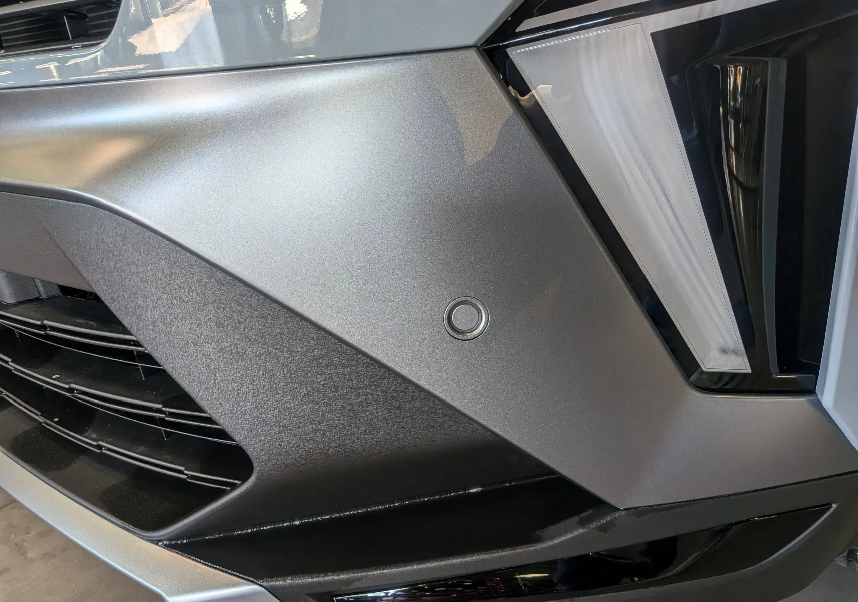 Détail du pare-chocs avant gris Rafale du Renault Symbioz E-TECH avec capteur de stationnement et optique LED.