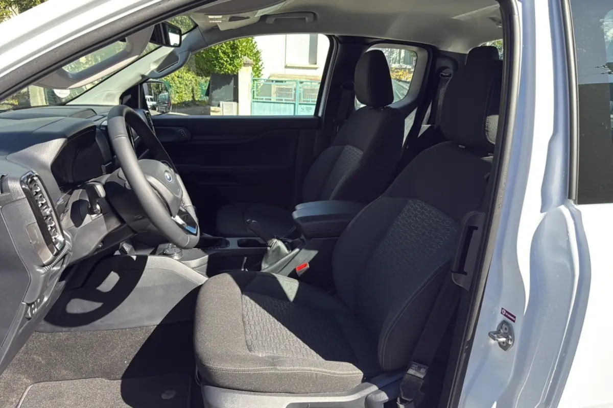 Vue intérieure côté conducteur du Ford Ranger blanc glacier 2025, montrant les sièges noirs et le volant multifonctions en cuir.