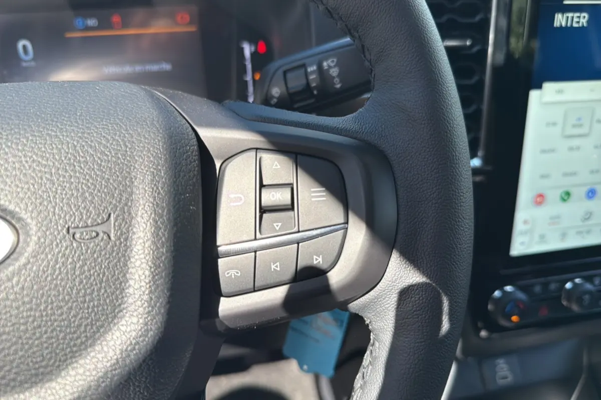 Gros plan sur le volant cuir multifonctions du Ford Ranger blanc glacier, avec commandes audio et écran tactile en arrière-plan.
