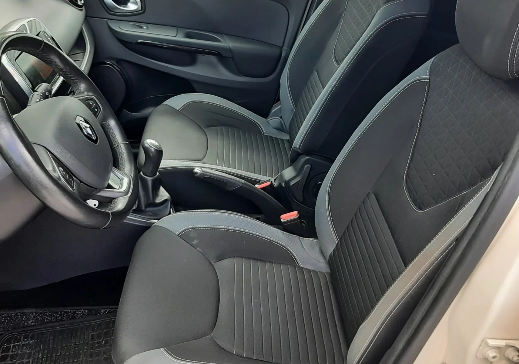 Vue intérieure côté conducteur de la Renault Clio IV Estate beige, avec sièges tissu noir et volant multifonction.