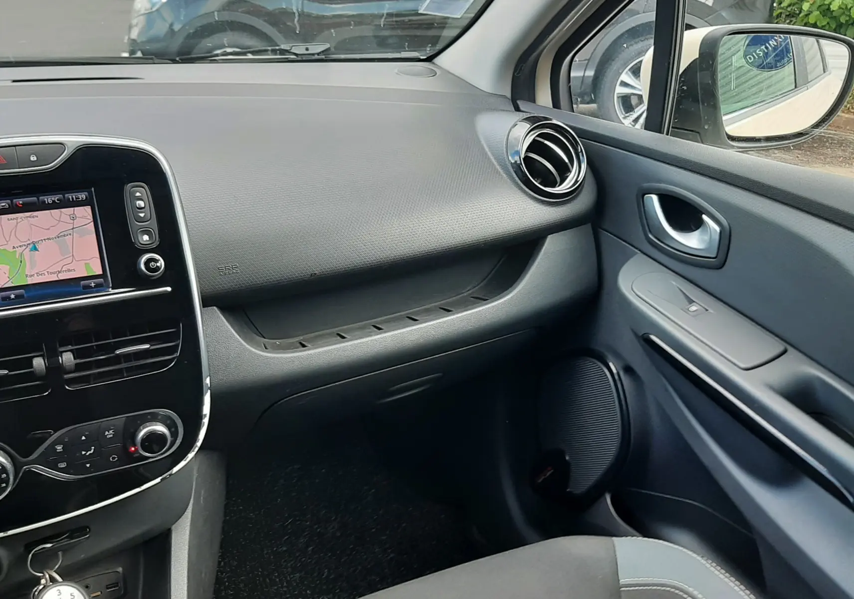 Vue intérieure côté passager de la Renault Clio IV Estate beige, montrant tableau de bord et console centrale avec navigation.