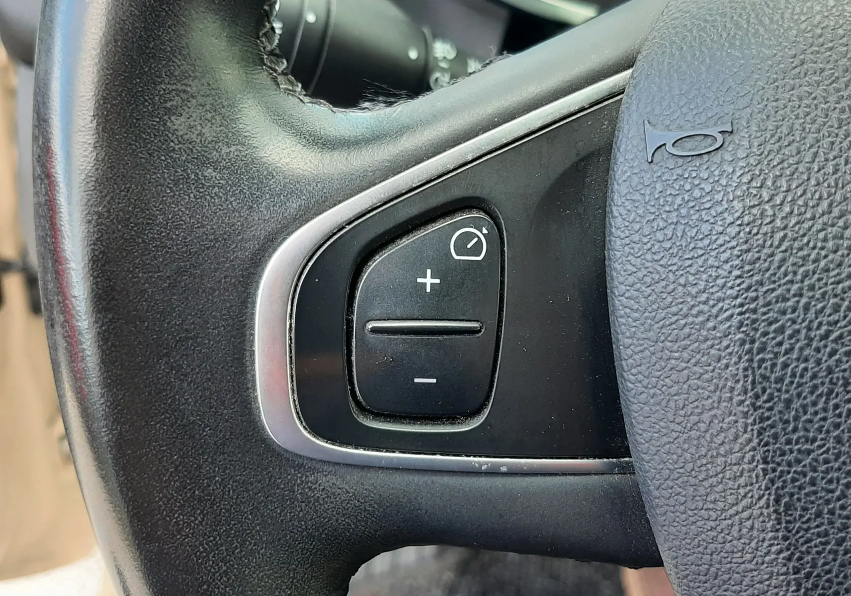 Gros plan sur les commandes de régulateur de vitesse sur le volant noir d'une Renault Clio IV Estate beige de 2016.