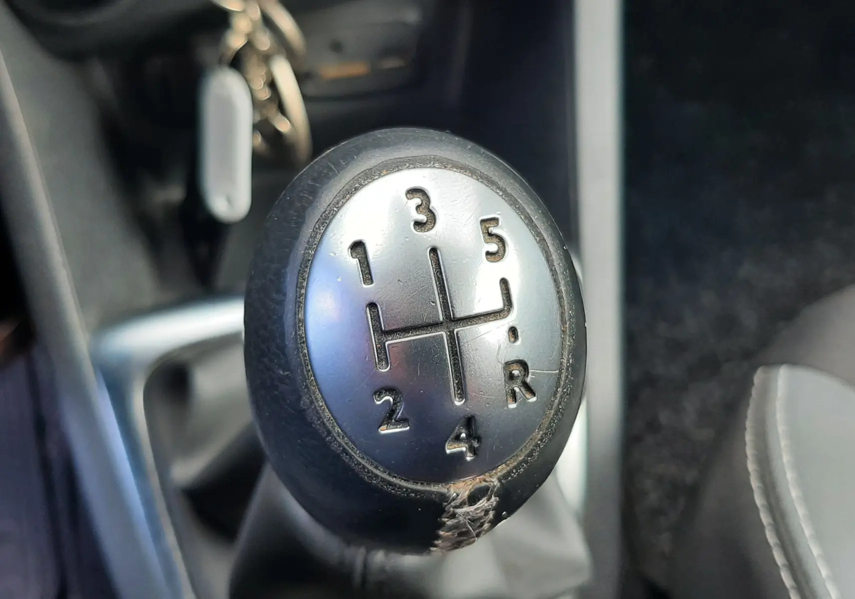 Gros plan sur le levier de vitesse manuel noir et argenté de la Renault Clio IV Estate beige, intérieur tissu noir.