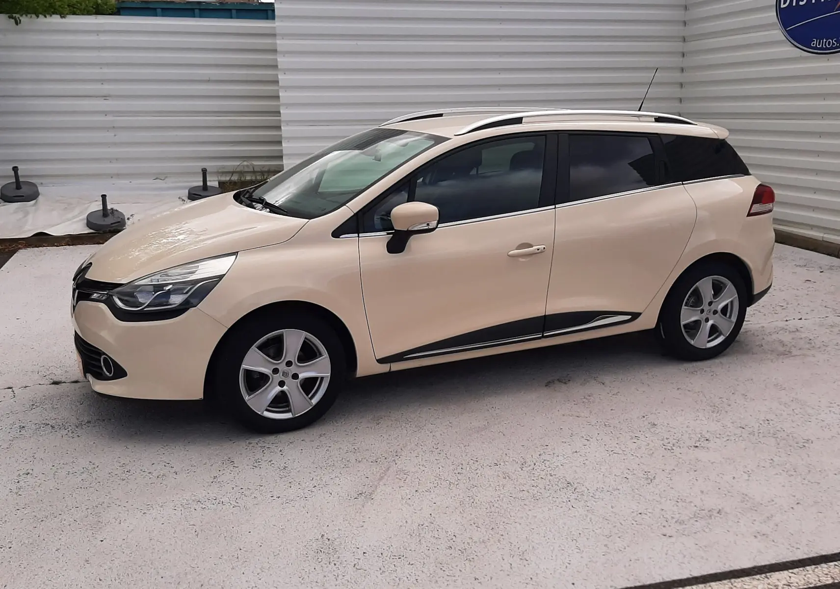 Renault Clio IV Estate beige vue de profil côté gauche, avec barres de toit et jantes alliage 5 branches.