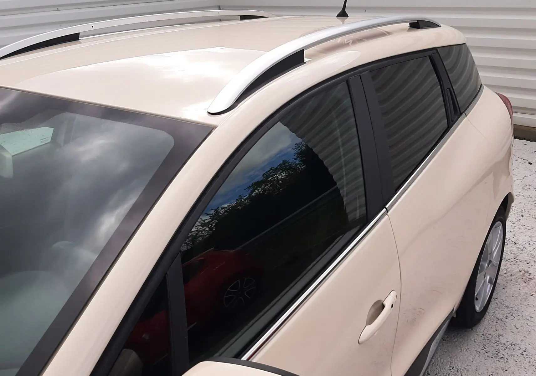 Vue 3/4 avant droit d'une Renault Clio IV Estate beige avec barres de toit et vitres teintées.