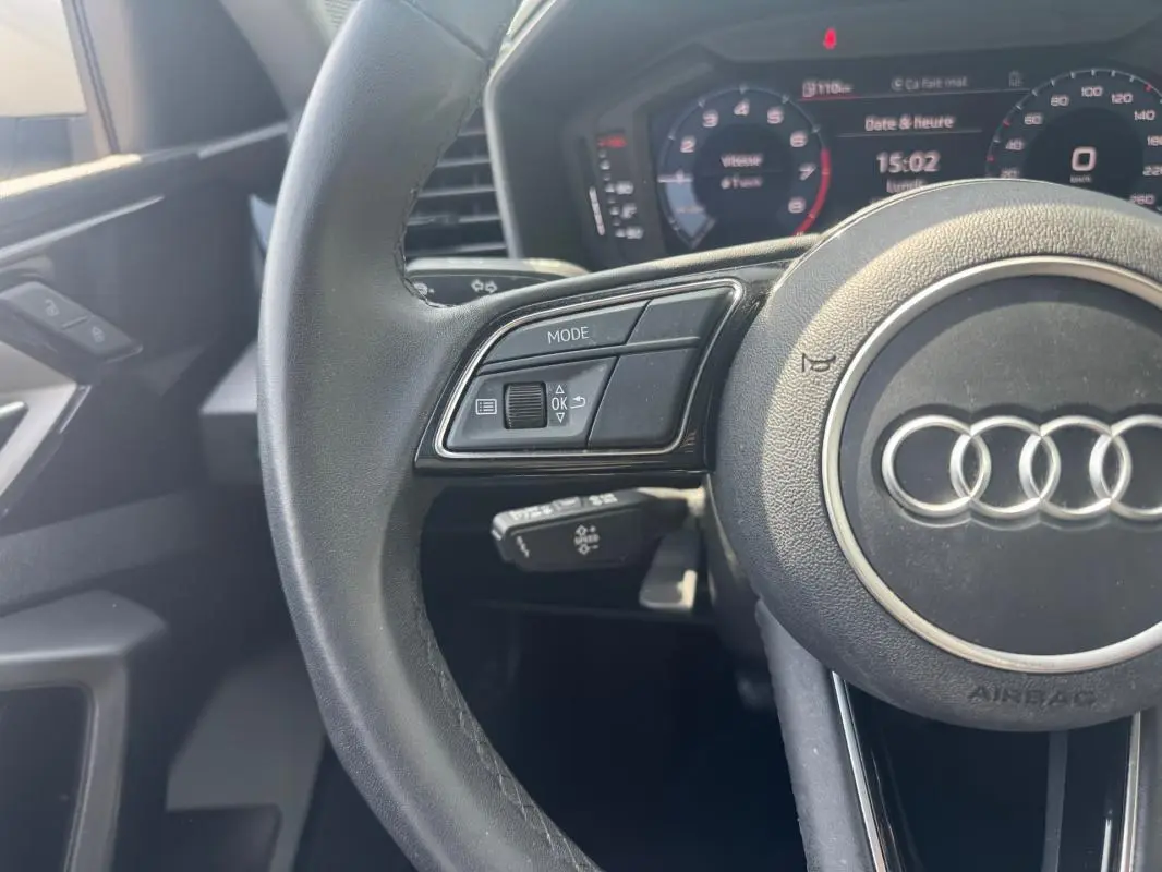 Vue rapprochée du volant cuir noir d'une Audi A1 Sportback 2025 avec commandes intégrées et cockpit numérique en arrière-plan.