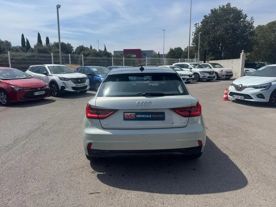 Vue arrière d'une Audi A1 Sportback gris clair 2025 avec feux LED et vitre arrière teintée, stationnée en extérieur.