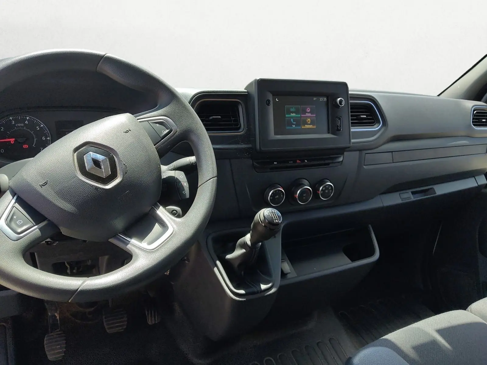 Vue intérieure côté conducteur du tableau de bord noir du Renault Master blanc avec volant, écran tactile et levier de vitesse manuel.