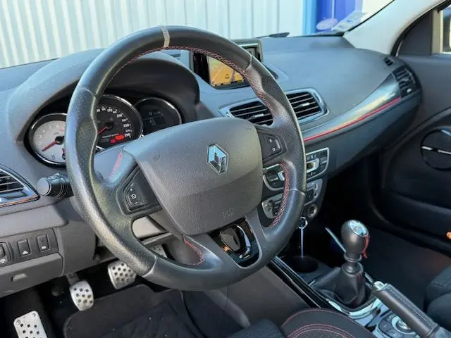 Intérieur de Renault Mégane III Coupé 2.0T blanc nacré, vue sur volant cuir perforé, tableau de bord et levier de vitesse manuel.