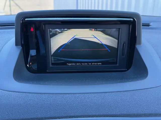 Écran de caméra de recul affichant la vue arrière avec lignes de guidage, dans une Renault Mégane III Coupé blanc nacré.