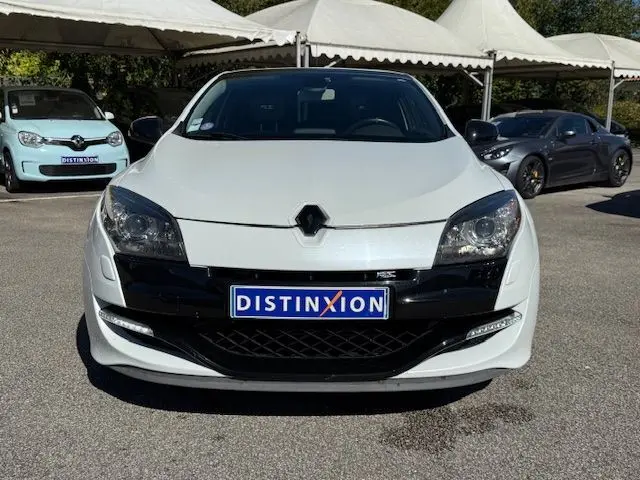 Vue frontale d'une Renault Mégane III Coupé 2.0T RS blanc nacré avec calandre noire et phares Xenon visibles.