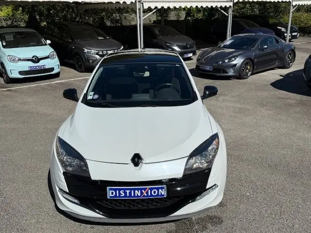 Vue avant d'une Renault Mégane III Coupé 2.0T RS blanc nacré, avec calandre noire et plaque Distinxion visible.