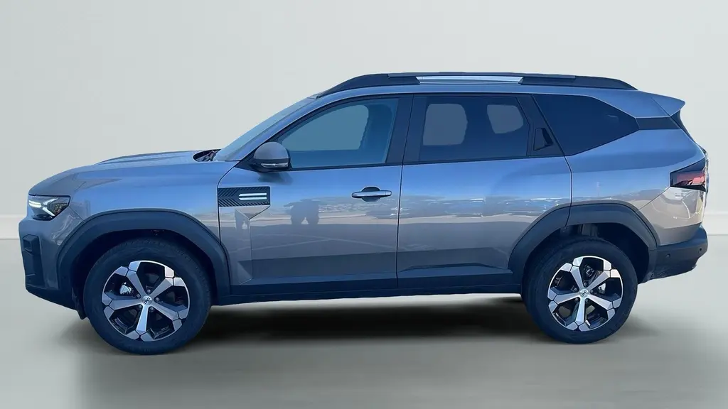 Vue de profil côté gauche du SUV Dacia Bigster 155 Journey gris schiste avec jantes alliage diamantées et barres de toit longitudinales.