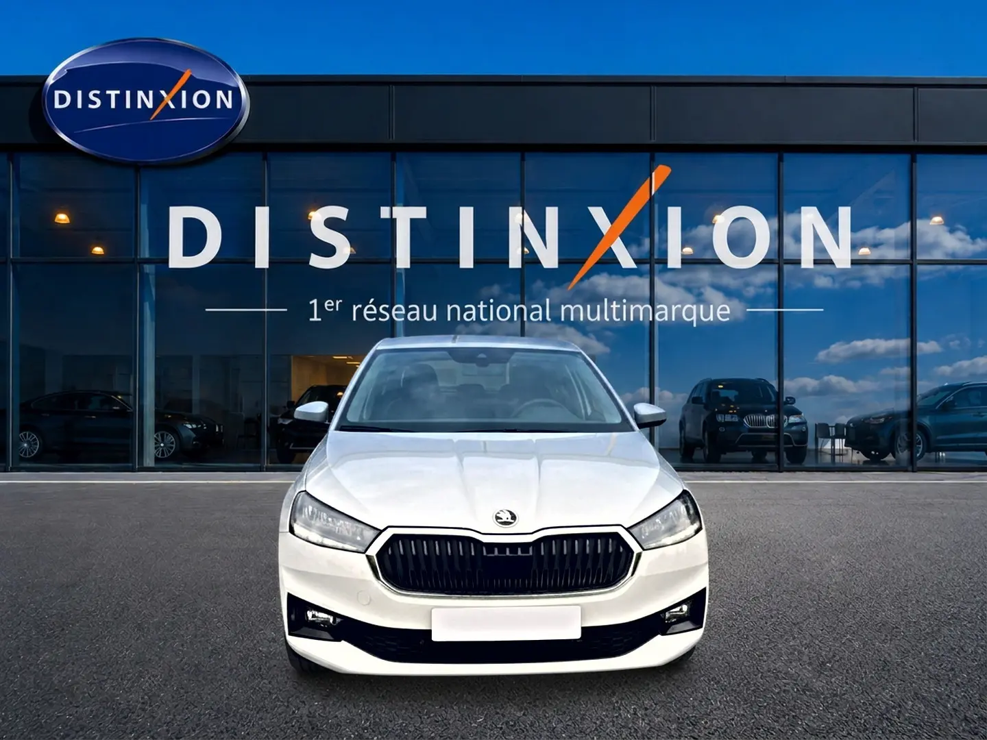 Vue avant d'une Skoda Fabia blanche 2025 avec calandre noire, stationnée devant une vitrine Distinxion.