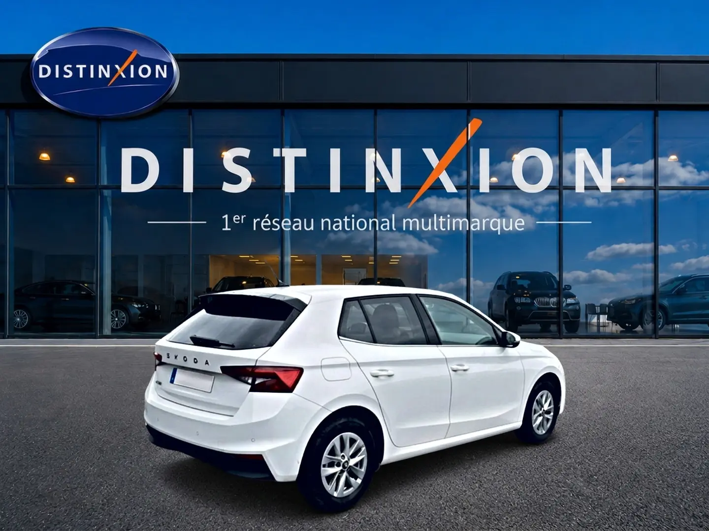Vue 3/4 arrière droite d'une Skoda Fabia blanche 2025 avec jantes alu, stationnée devant un showroom Distinxion.