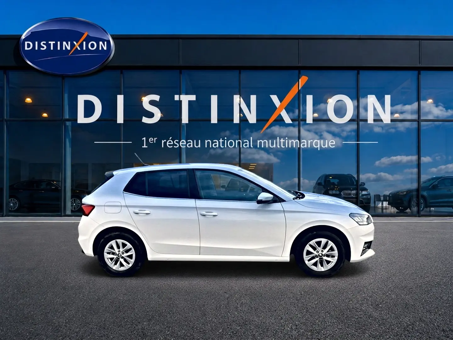 Vue latérale droite d'une Skoda Fabia blanche 2025 garée devant une vitrine avec logo Distinxion.