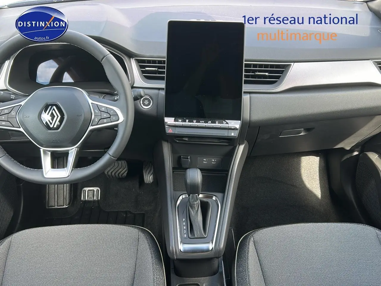 Vue intérieure avant du Renault Captur 2025 avec écran tactile vertical, volant multifonction et levier de boîte auto.