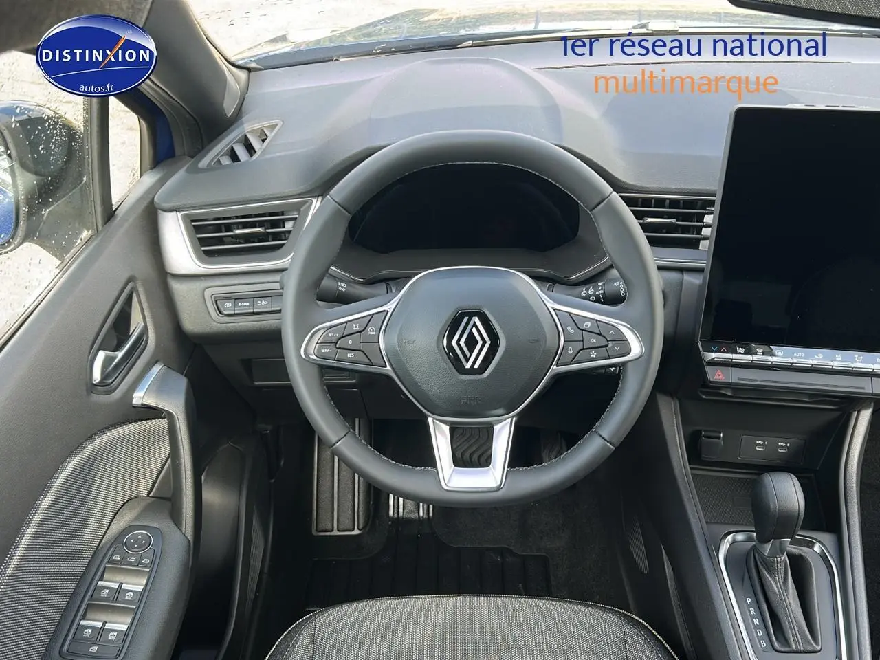 Vue intérieure centrée sur le volant multifonction du Renault Captur bleu iron, avec écran tactile et levier de vitesses automatique visible.