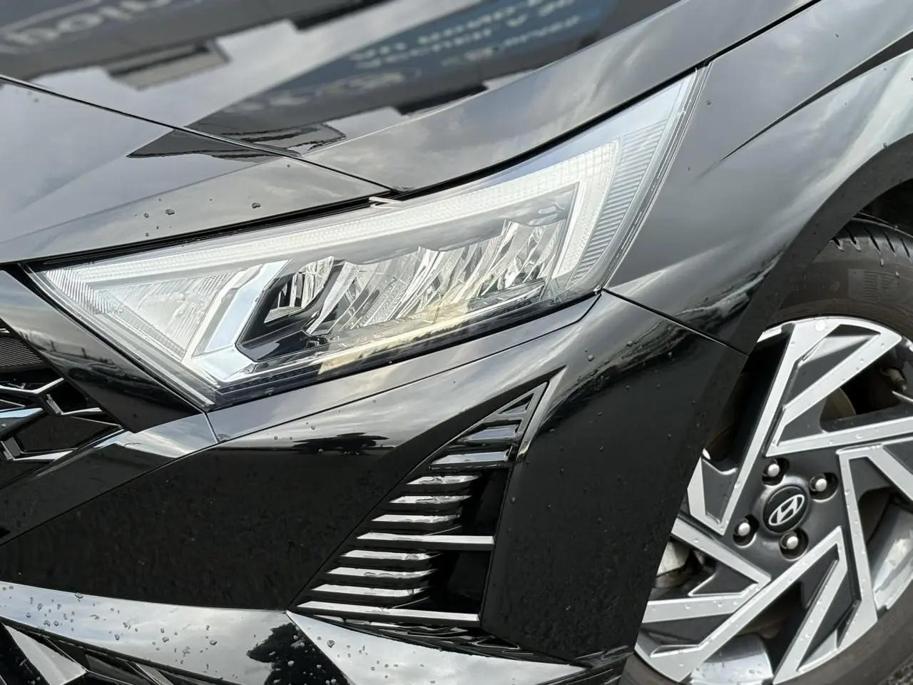 Gros plan sur l'avant droit noir Phantom Metal de la Hyundai i20 2025, mettant en valeur le phare et la jante alliage diamantée.