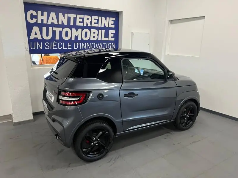 Vue 3/4 arrière droite de la Ligier JS50 Sport Elite E5+ gris avec toit noir et jantes noires en intérieur showroom.