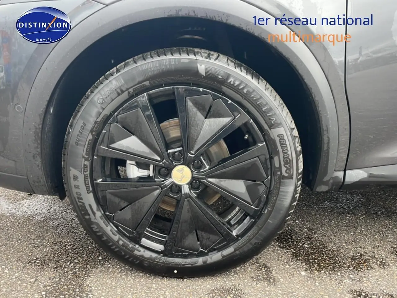 Gros plan sur la roue avant droite du DS7 gris titane, mettant en valeur la jante alu noire au design géométrique.