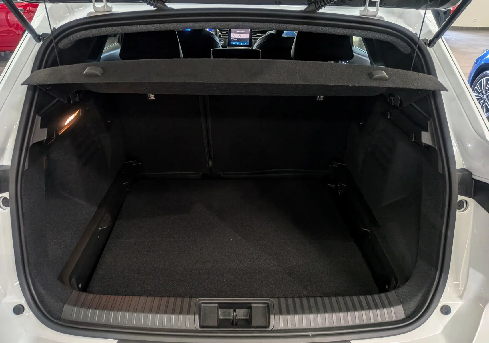 Coffre ouvert vu de l'arrière d'une Renault Symbioz blanc nacré, intérieur noir avec tablette cache-bagages déployée.