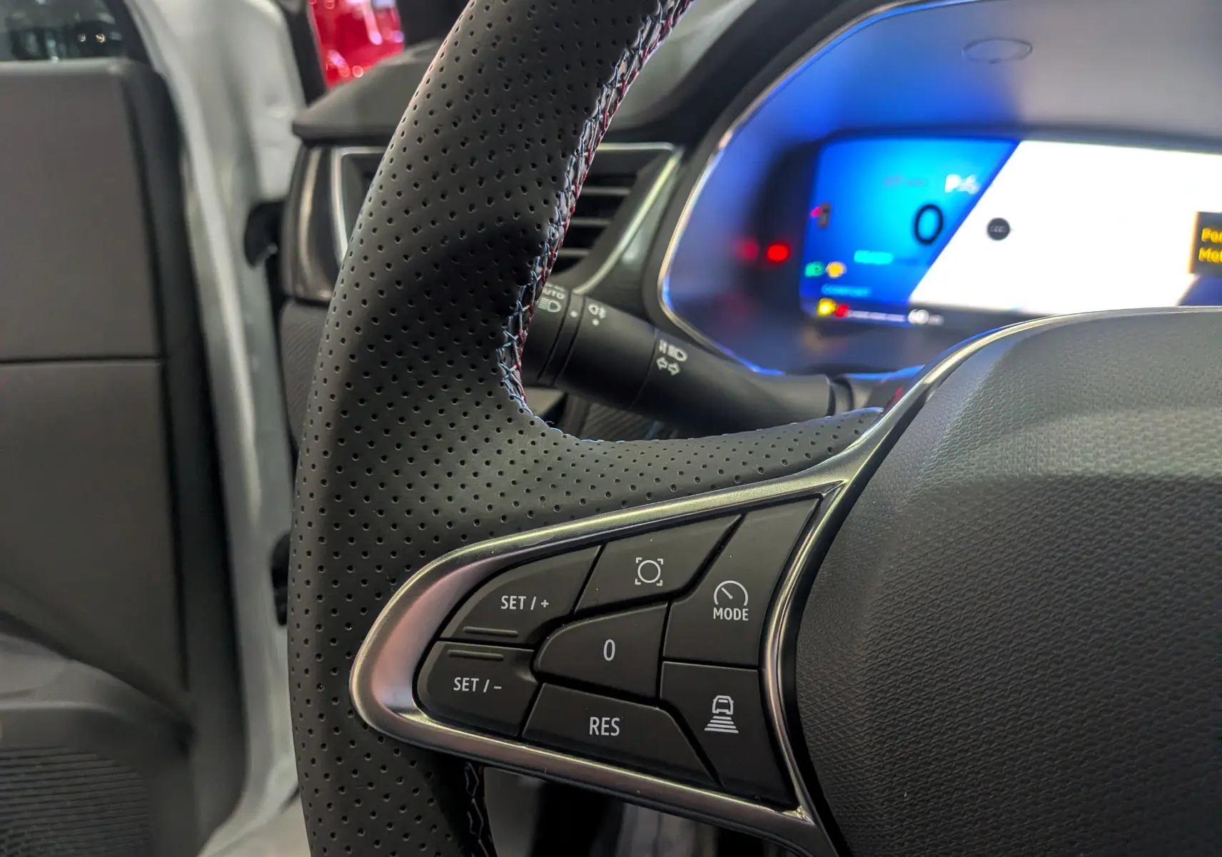Gros plan sur la partie gauche du volant perforé noir du Renault Symbioz 2026 avec tableau de bord digital bleu en arrière-plan.
