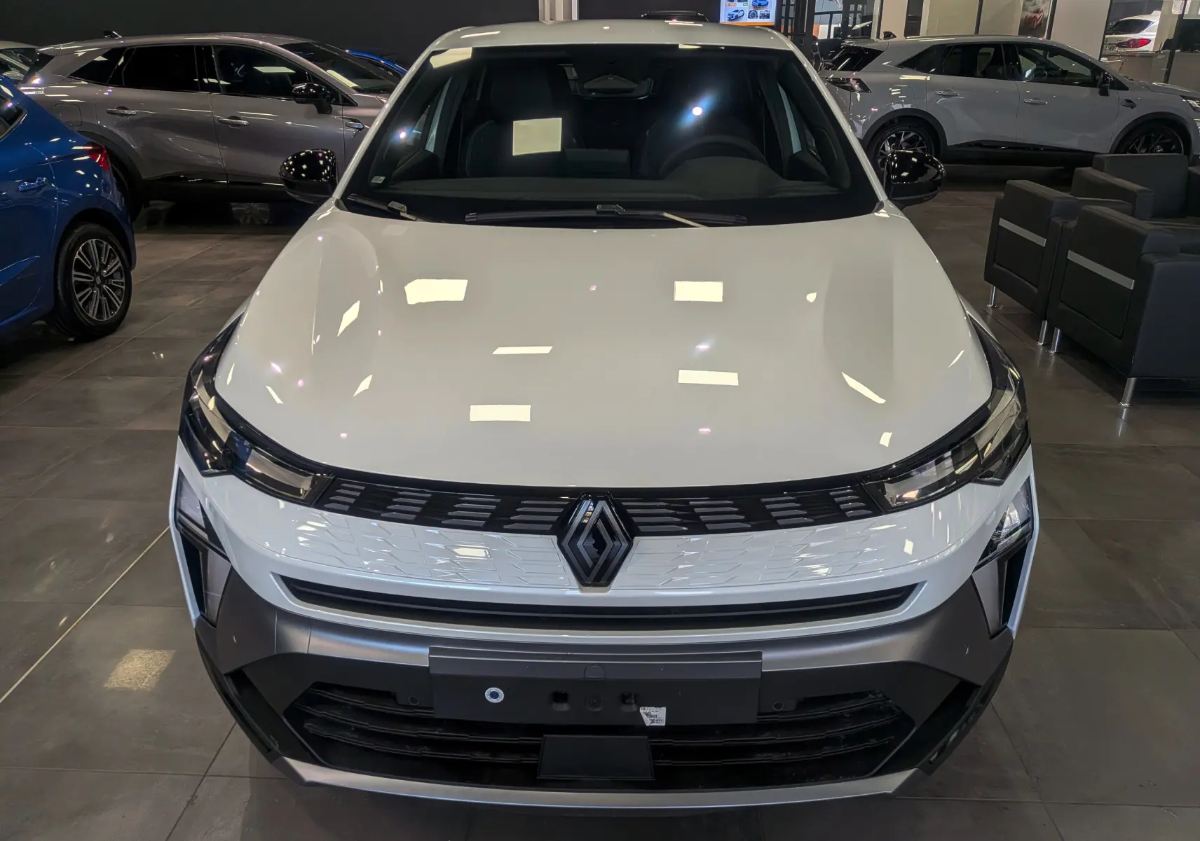 Vue frontale d'une Renault SYMBIOZ blanc nacré en showroom, avec calandre noire et logo Renault central bien visible.