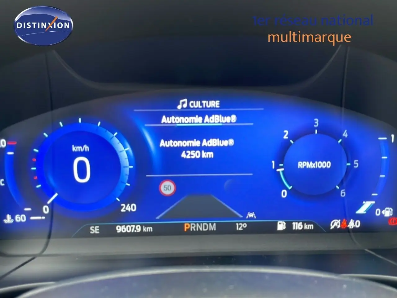 Vue du tableau de bord numérique du Ford Kuga 2024, affichage bleu avec vitesse, régime moteur et autonomie AdBlue.