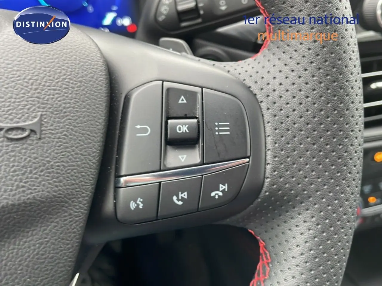 Gros plan sur le volant en cuir perforé noir avec surpiqûres rouges du Ford Kuga 2024, boutons de commande visibles.