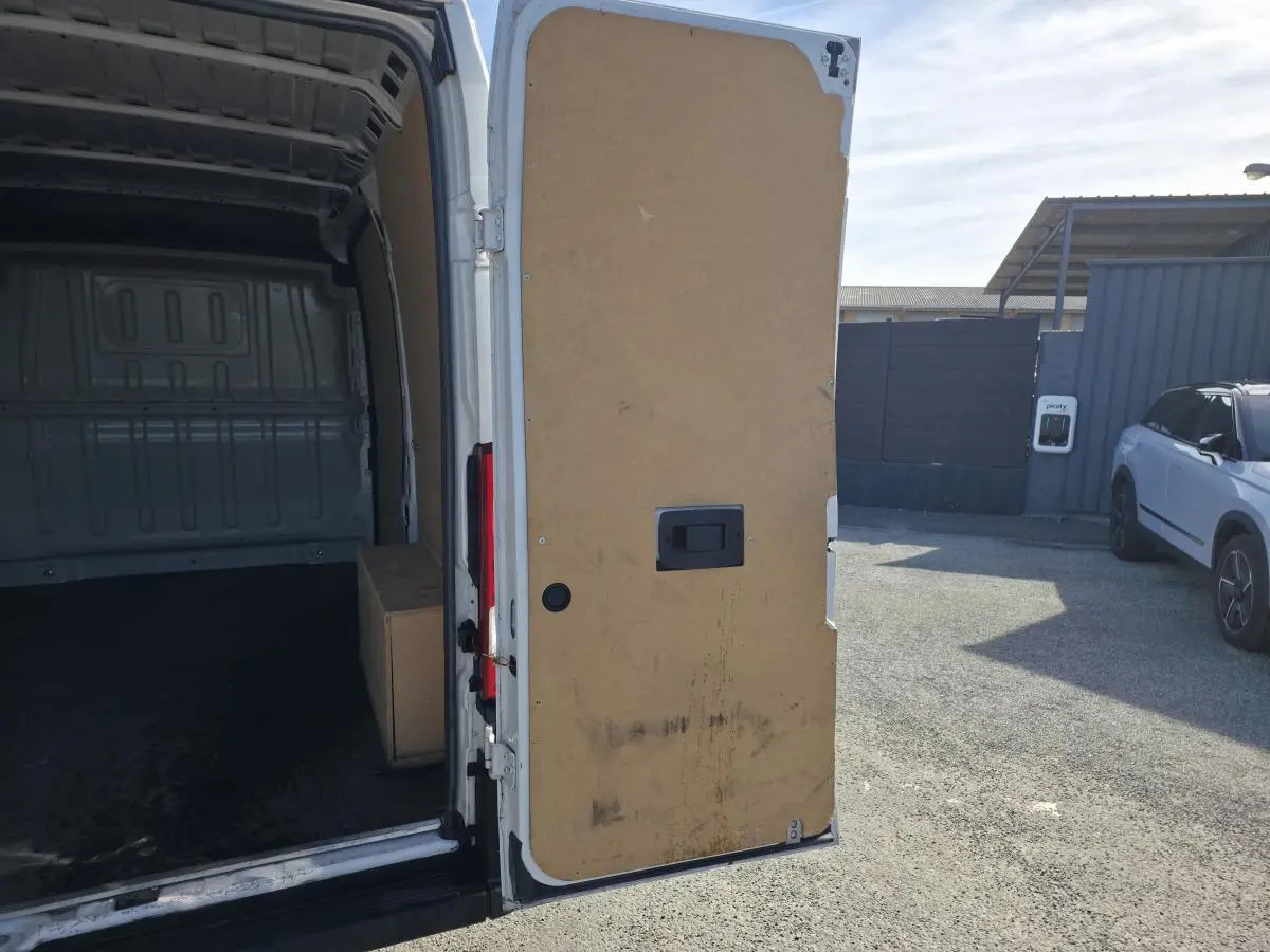 Vue arrière droite d'un FIAT Ducato Fourgon blanc 2023 avec porte arrière tôlée ouverte montrant l'intérieur vide.