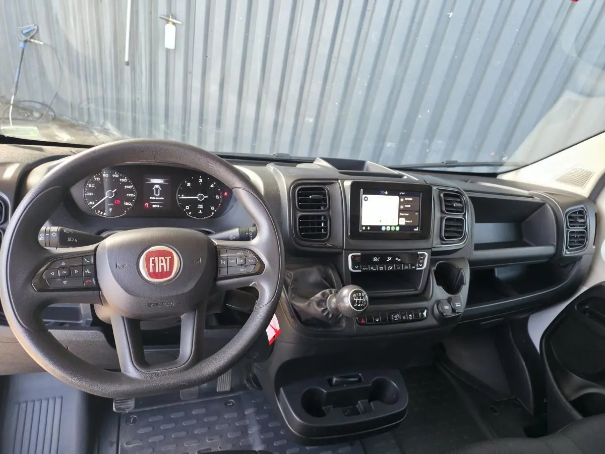 Vue intérieure du tableau de bord du Fiat Ducato Fourgon 2023, volant, écran tactile et levier de vitesses manuelle visibles.