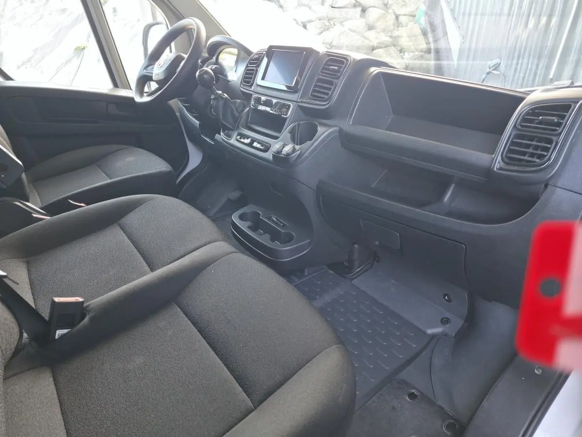 Vue intérieure côté conducteur du Fiat Ducato Fourgon 2023, montrant sièges noirs et tableau de bord avec écran tactile.