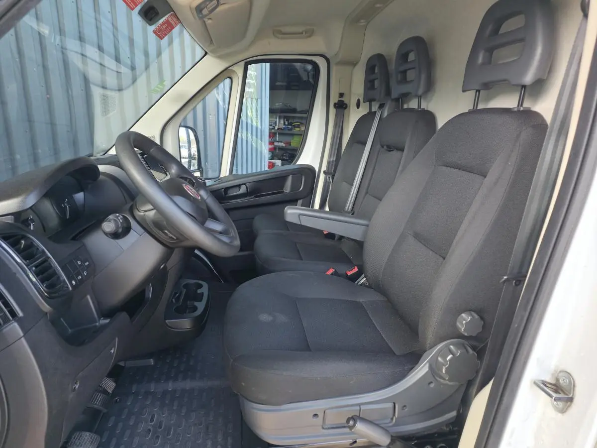 Vue intérieure côté conducteur du Fiat Ducato Fourgon blanc 2023, montrant les sièges noirs et le volant avec tableau de bord.
