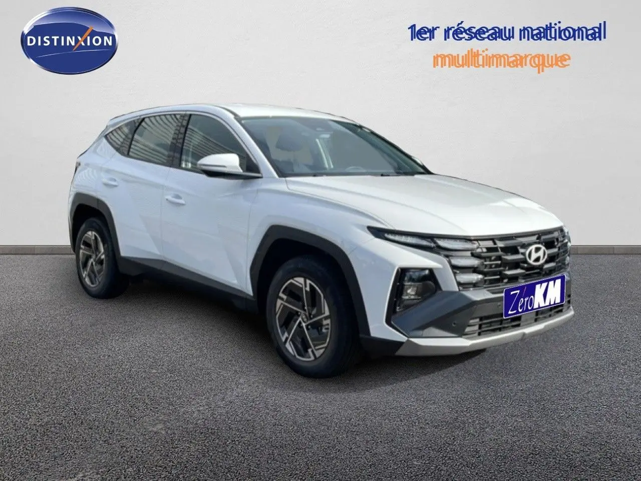 Vue 3/4 avant d'un Hyundai Tucson blanc Atlas 2026 avec calandre noire et jantes modernes sur sol gris.