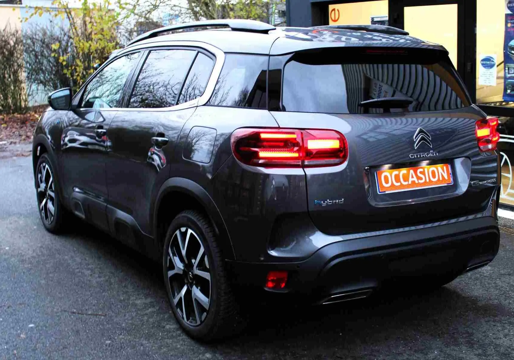 Vue 3/4 arrière droite d'un Citroën C5 Aircross gris platinium avec feux arrière allumés et badge hybride visible.
