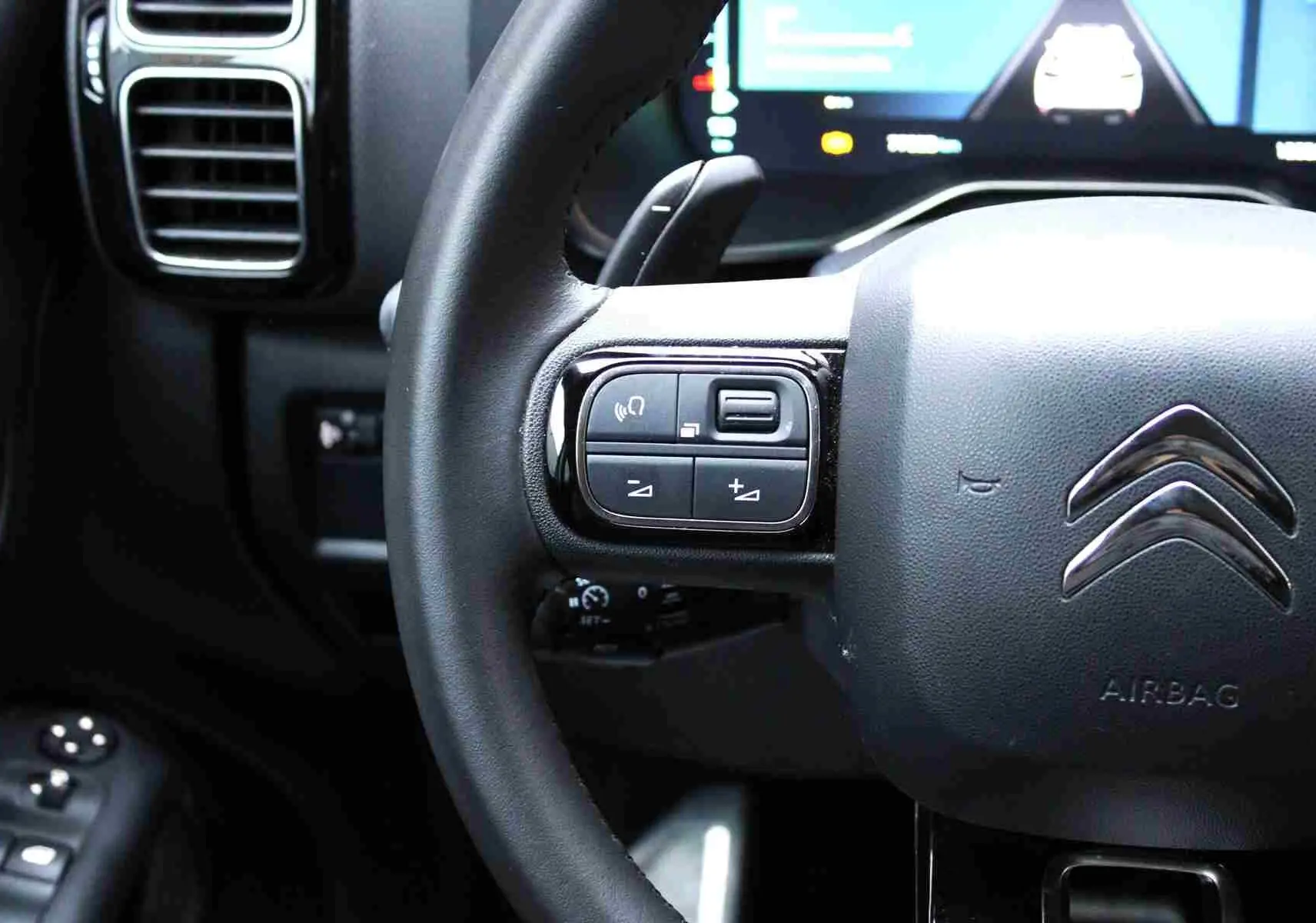 Gros plan sur le volant cuir du Citroën C5 Aircross hybride, avec commandes intégrées et tableau de bord numérique en arrière-plan.
