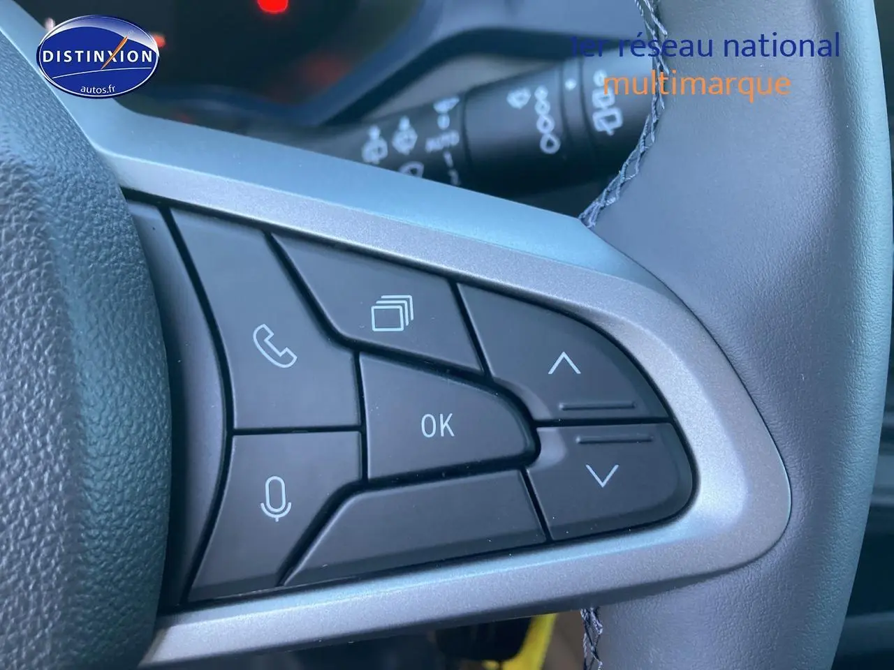 Gros plan sur les commandes multifonctions noires du volant du Dacia Duster 2025, avec boutons de navigation et appel.