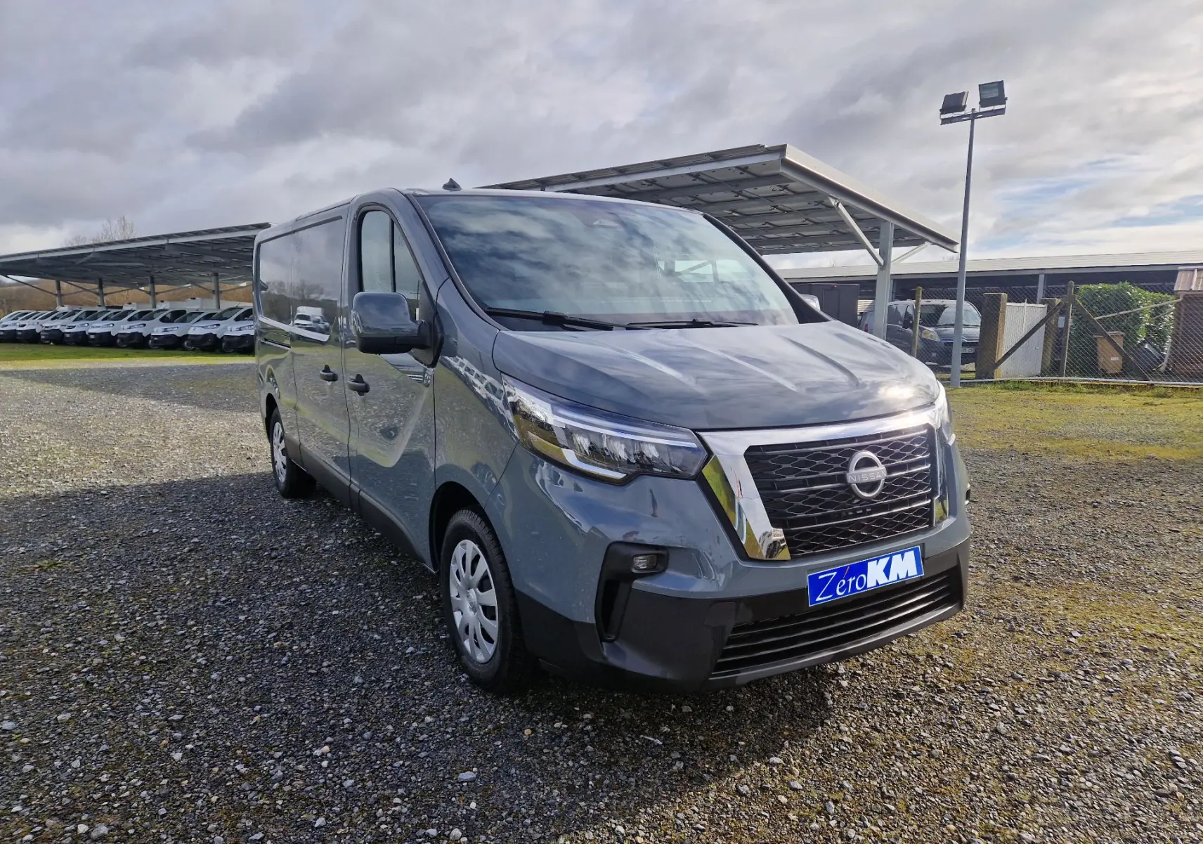 Nissan Primastar gris urbain en 3/4 avant droit, avec calandre chromée et plaque "Zero KM" visible.