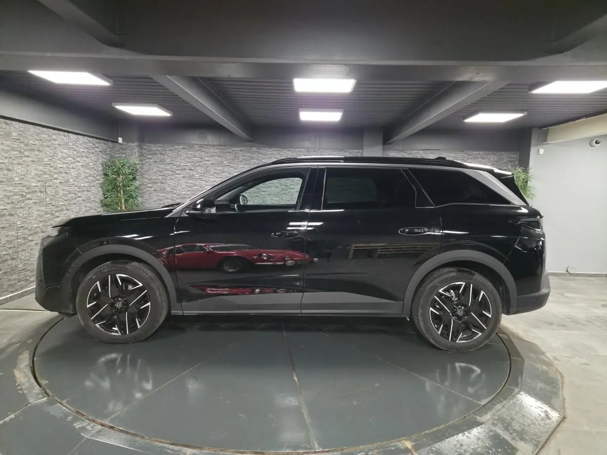 Vue de profil côté gauche d’un Peugeot 5008 noir 2025 avec jantes alliage 19 pouces et barres de toit noires.