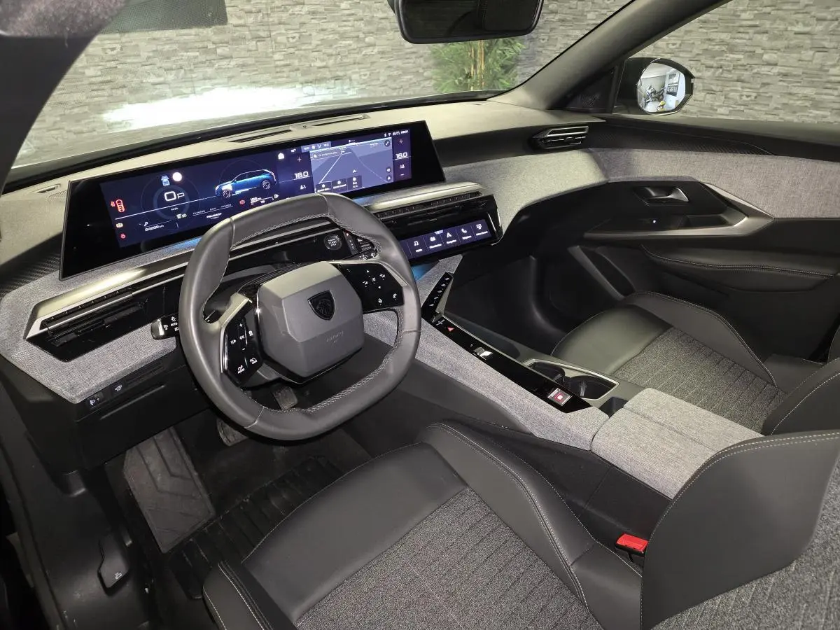 Vue intérieure côté conducteur du Peugeot 5008 2025 hybride, volant compact cuir noir et tableau de bord numérique panoramique.