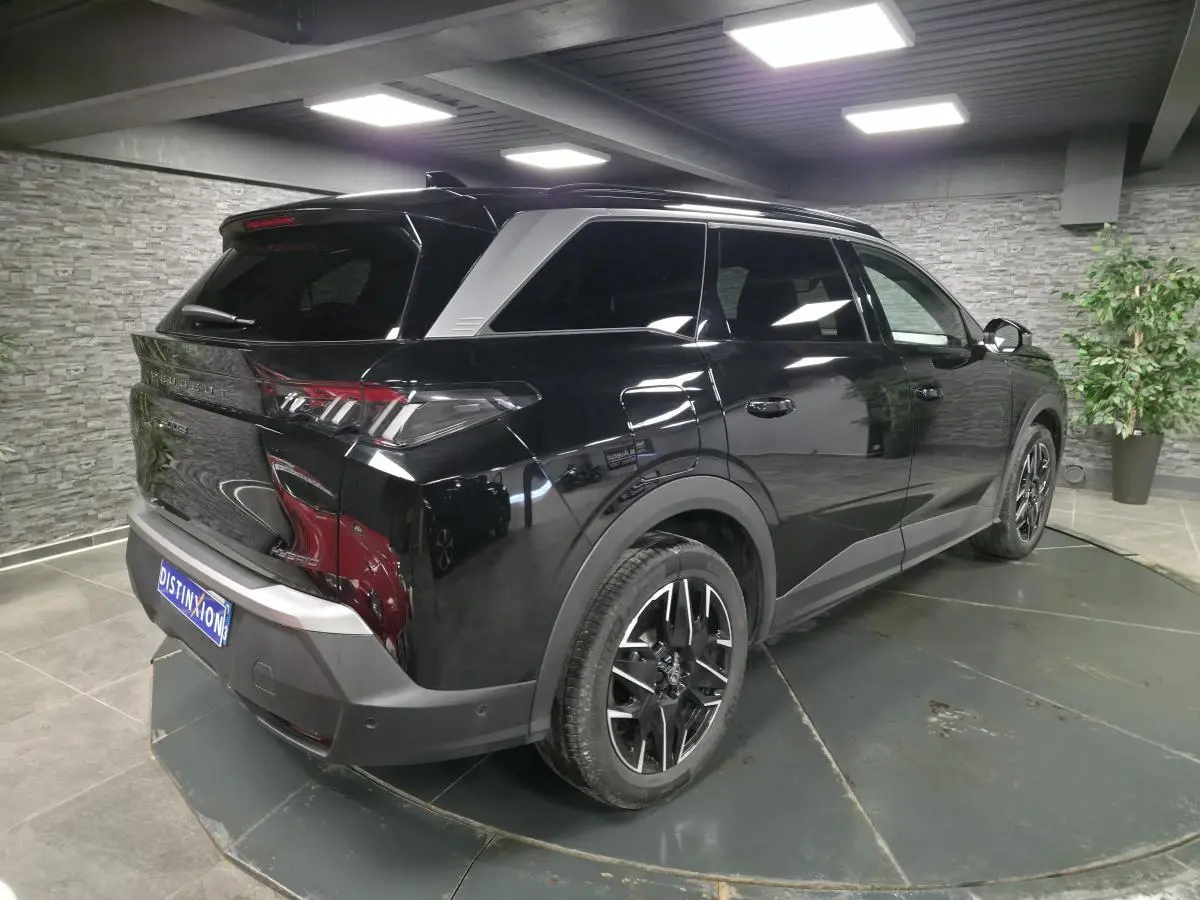 Vue 3/4 arrière droite du Peugeot 5008 noir 2025 avec jantes alliage 19'' et barres de toit noires brillantes.