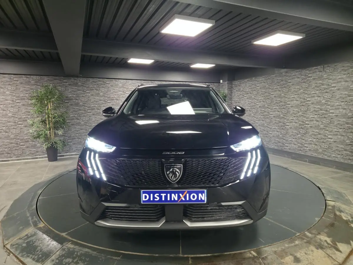 Vue frontale d'un Peugeot 5008 noir 2025 avec feux LED allumés et calandre noire brillante dans un showroom.